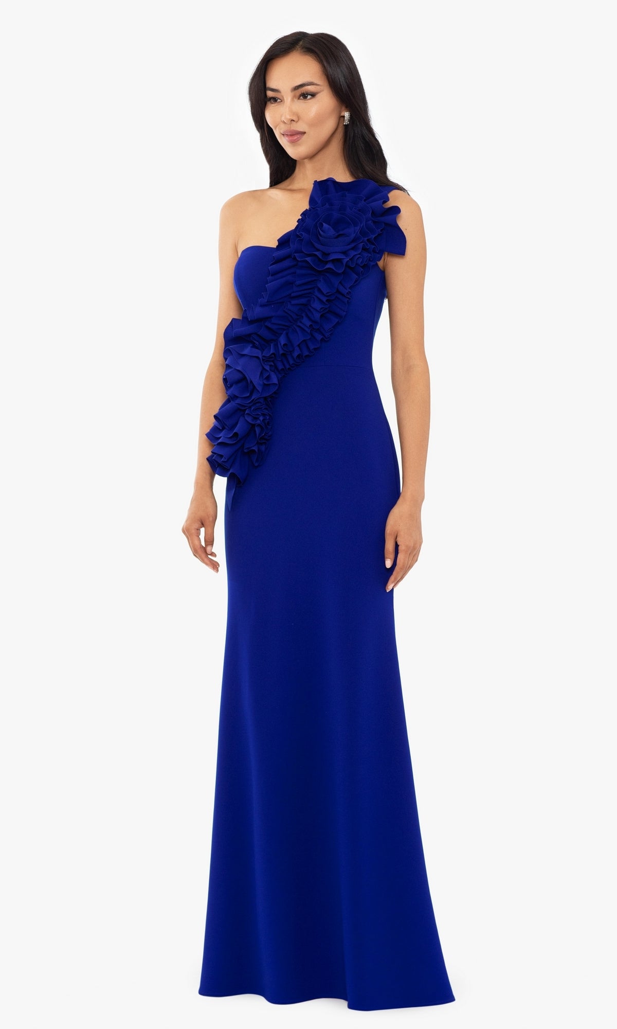 A woman stands against a white background, wearing the Betsy and Adam One-Shoulder Long Prom Dress A26071 in royal blue, featuring elegant front ruffle detailing and a floor-length silhouette.